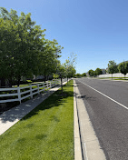 Long commercial park strip of mowed grass along a road and white fence