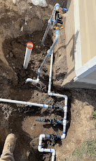 Sprinkler valves and PVC fittings plumbed in beside a house foundation